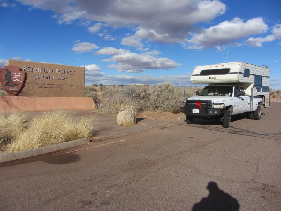 White 1997 Dodge 3500 pickup truck with a camper shell, parked near Petrified Forest National Park sign