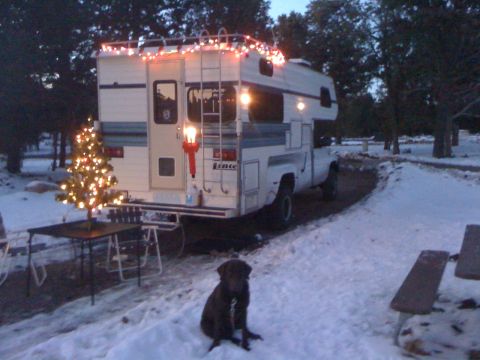 1997 Dodge 3500 - Truck camper with Christmas lights and tree in the snow. Dog sits nearby.