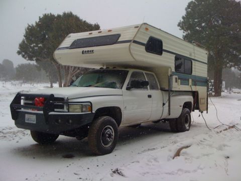 1997 Dodge 3500 - A white Dodge pickup truck with a camper shell is parked in a snowy landscape during winter.