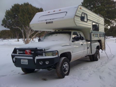 1997 Dodge 3500 - A white Dodge pickup truck with a Lance camper shell is parked in the snow, showing its front-right quarter view.