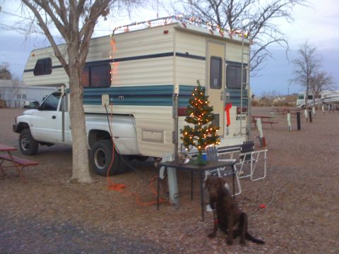 1997 Dodge 3500 - A white pickup truck with a camper shell is parked outdoors, decorated for Christmas with lights and a tree.