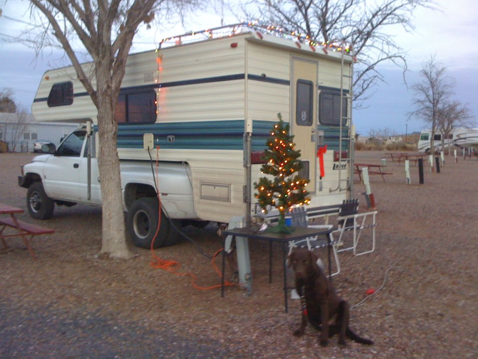 White pickup truck with a camper shell, seen from the front-left. The truck has dual rear wheels and appears to be from the mid-1990s