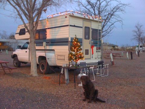 1997 Dodge 3500 - A white 1997 Dodge 3500 pickup truck with a camper shell is parked at a campsite, decorated with Christmas lights and a small tree.
