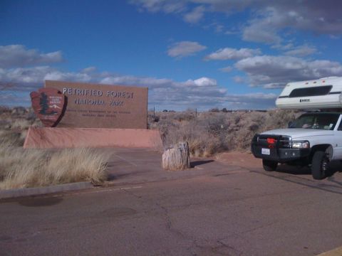 1997 Dodge 3500 - A white Dodge Ram pickup truck with a camper shell is parked near the entrance sign for Petrified Forest National Park.