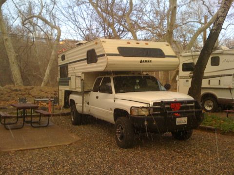 1997 Dodge 3500 - A white Dodge pickup truck with a Lance camper shell is parked next to another RV in a campground.