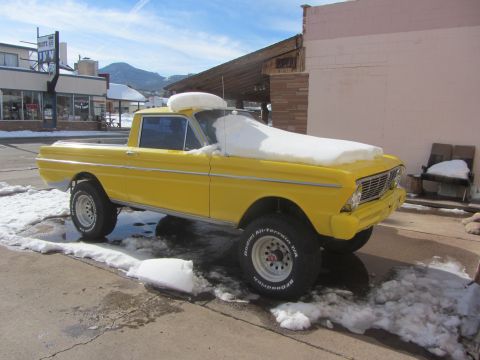 1964 Ford Ranchero - Yellow 1964 Ford Ranchero covered in snow, parked on a street with buildings in the background.