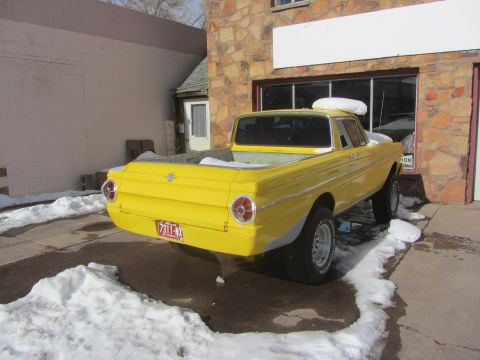 1964 Ford Ranchero - This yellow pickup truck is parked in front of a stone building with snow on the ground.