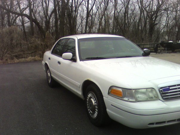 White Ford Crown Victoria sedan, front three-quarter passenger view, parked near bare trees