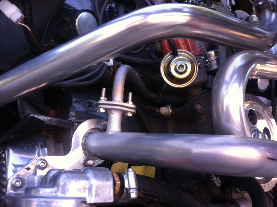 Close-up of a vehicle's engine bay, showing shiny custom exhaust pipes, distributor cap, and wiring