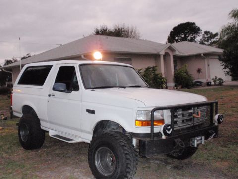 1995 Ford Bronco - White 1995 Ford Bronco with aftermarket bull bar and large off-road tires parked in front of a house.