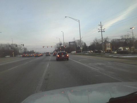 2003 Ford Crown Victoria - Vehicles navigate a road with traffic signals and overhead wires under a cloudy sky.