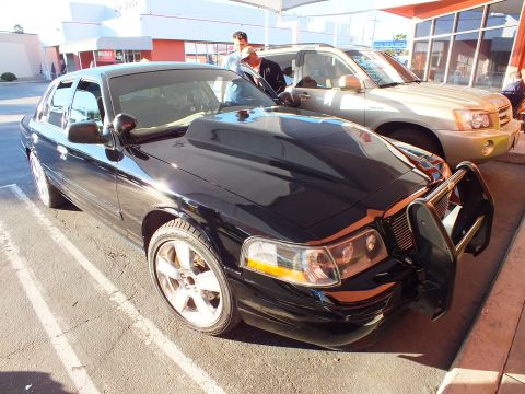 2003 Ford Crown Victoria - Customized black sedan with grille guard parked beside an SUV at a detail shop.