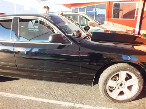 2003 Ford Crown Victoria - Side profile of a glossy black sedan showing tinted glass and a chrome wheel.