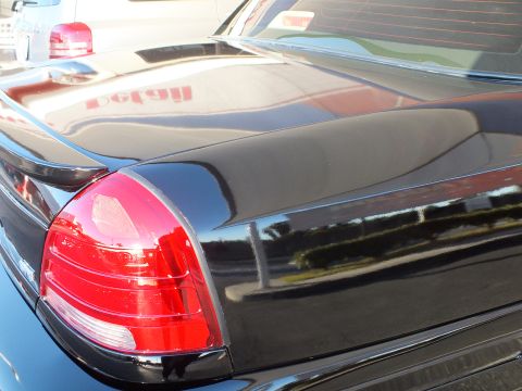2003 Ford Crown Victoria - Detail of the rear tail lamp and decklid lip spoiler on a glossy black sedan.