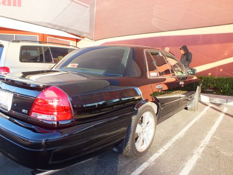 2003 Ford Crown Victoria - Black sedan parked rear-three-quarter with a person standing at the open driver door.