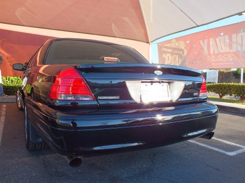 2003 Ford Crown Victoria - Black Crown Victoria sedan tail end showing taillights and chrome bumper, shop canopy overhead.