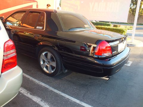 2003 Ford Crown Victoria - Rear quarter of a lowered black Crown Victoria sedan on polished alloys, parked by another car.