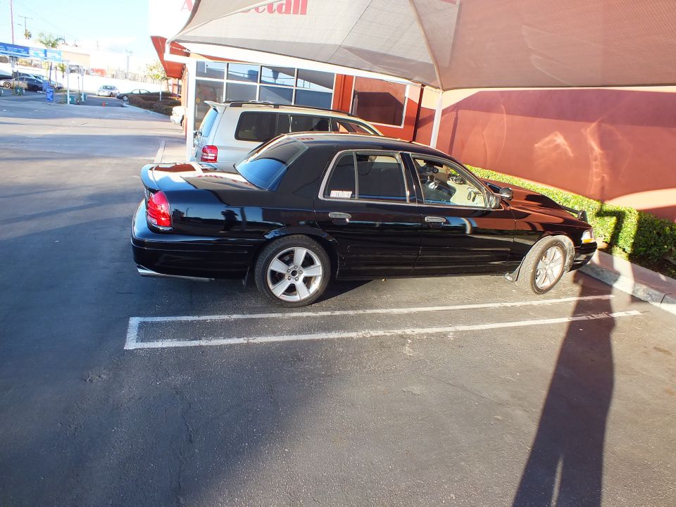 Black Crown Victoria profile right side parked in striped lot near storefront