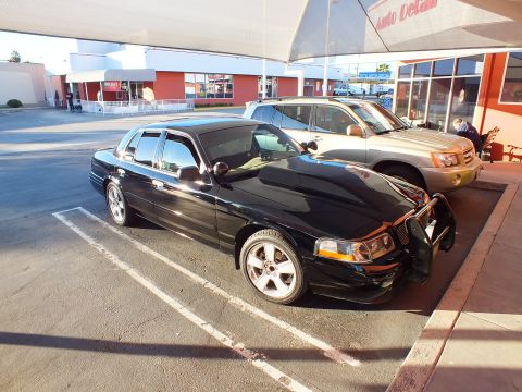 2003 Ford Crown Victoria - Front-left of a black Crown Victoria fitted with a push bar, parked by an SUV at a shop.