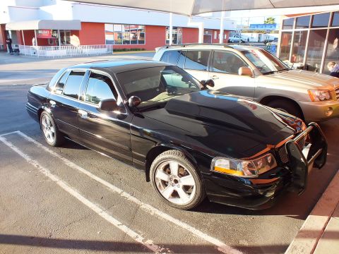 2003 Ford Crown Victoria - Front quarter of a black Crown Victoria on alloy wheels with brush guard, shop in background.