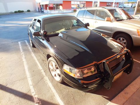 2003 Ford Crown Victoria - Elevated front-left view of a black Crown Victoria with push bar and amber turn signals.