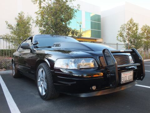 2003 Ford Crown Victoria - Front-right view of a black Crown Victoria with push bar and billet grille, building behind.
