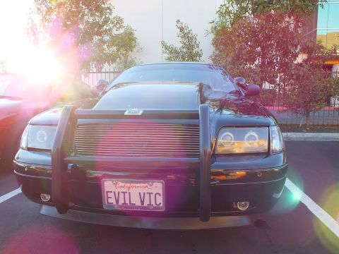 2003 Ford Crown Victoria - Front of a black Crown Victoria with brush guard and EVIL VIC plate, sunlight flaring left.