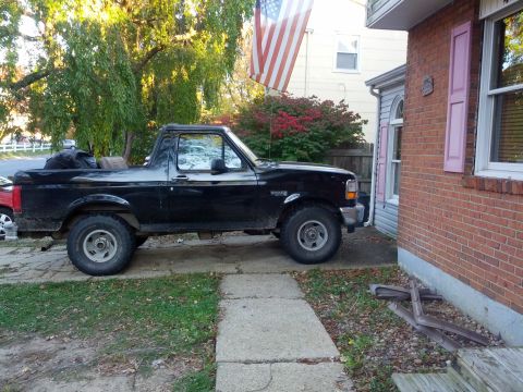 1995 Ford Bronco - A side view of a black 1995 Ford Bronco parked on a paved driveway next to a house.