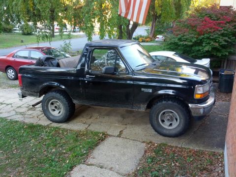 1995 Ford Bronco - This black Ford Bronco is parked on a driveway next to a red sedan and a white sports car.