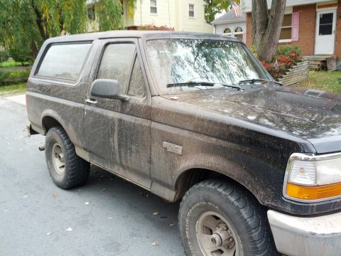 1995 Ford Bronco - This muddy black Ford Bronco is parked on a residential street.