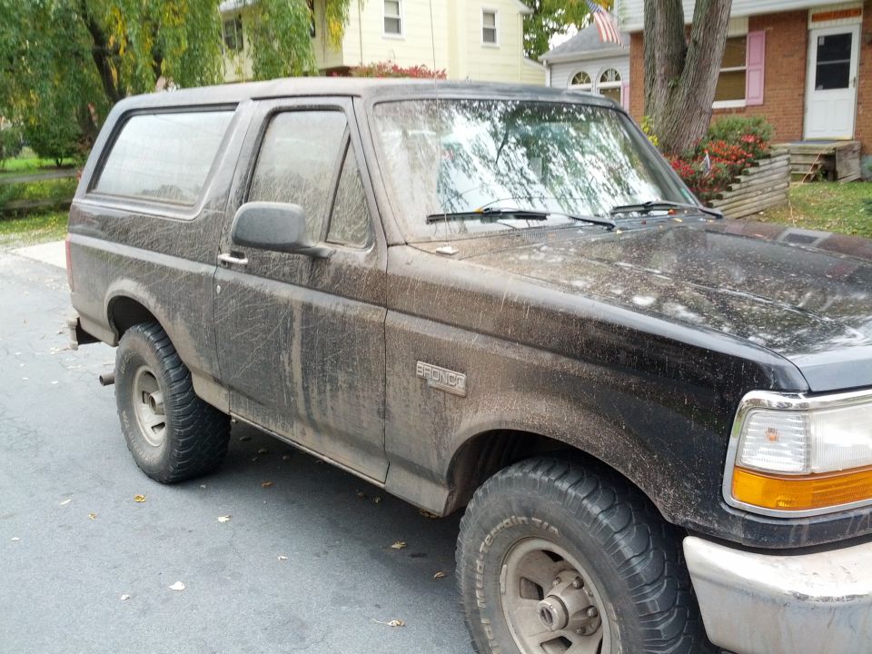 Black Ford Bronco covered in mud, parked on a street