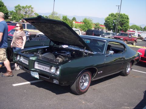 1972 Ford Ranchero - A classic dark green Pontiac Grand Prix is displayed with its hood open in a parking lot on a sunny day.