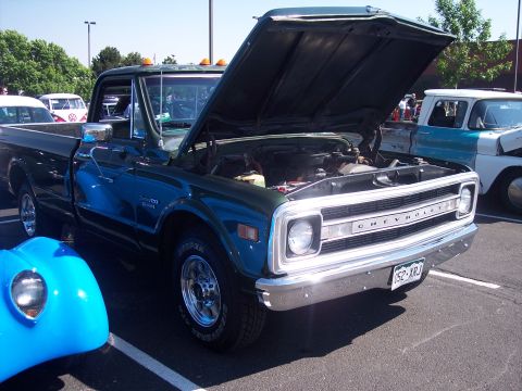 1972 Ford Ranchero - This dark green Chevrolet pickup truck is displayed with its hood open, revealing the engine bay. A blue vehicle is partially visible in th…