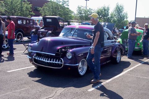 1972 Ford Ranchero - A man inspects a heavily customized purple coupe at an outdoor car show with other vehicles present.