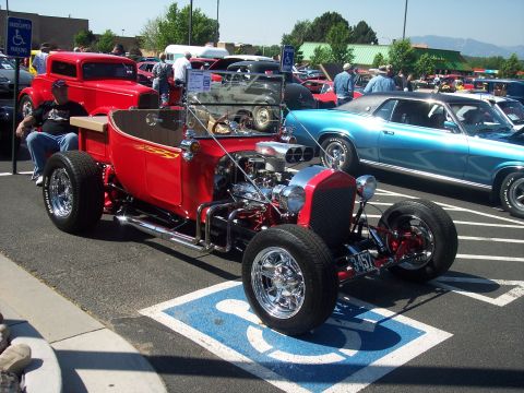 1972 Ford Ranchero - A custom red hot rod with a powerful engine is parked in a handicapped spot at an outdoor event.
