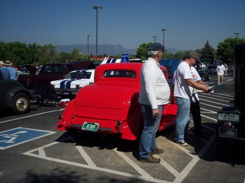 1972 Ford Ranchero - A red coupe hot rod is parked in a lot with other vehicles, and people are gathered around.