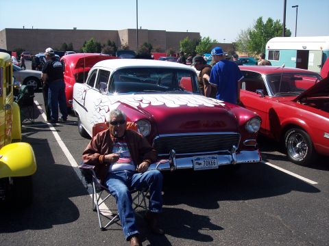 1972 Ford Ranchero - Man relaxes near a classic 1955 Chevrolet Bel Air at a car show, with other vehicles present.