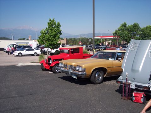1972 Ford Ranchero - A gold sedan is parked with its hood open, displaying a trophy and a red bag nearby, alongside other vehicles.