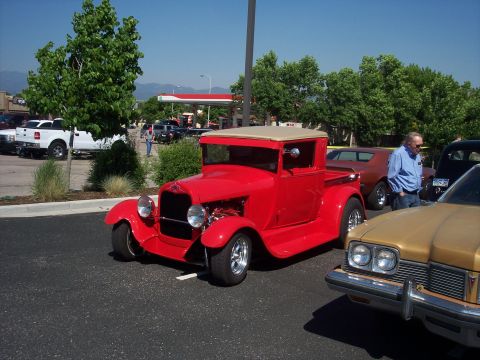 1972 Ford Ranchero - A classic red pickup truck is parked at an outdoor event with other vehicles and a man observing.