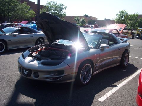 1972 Ford Ranchero - Silver 1998 Pontiac Firebird Trans Am at a car show, hood open, parked in a lot.