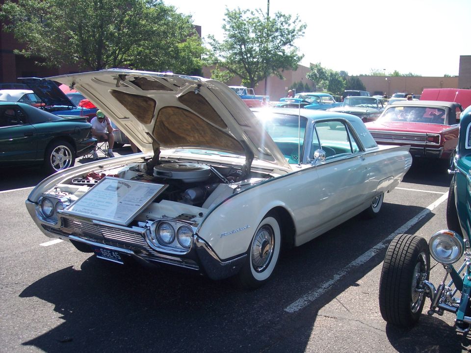 White 1961 Ford Thunderbird with hood open, parked at a car show