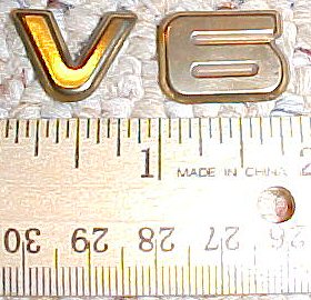 2003 Ford Expedition - Two V6 emblems are shown next to a ruler for scale. Text on ruler is visible.