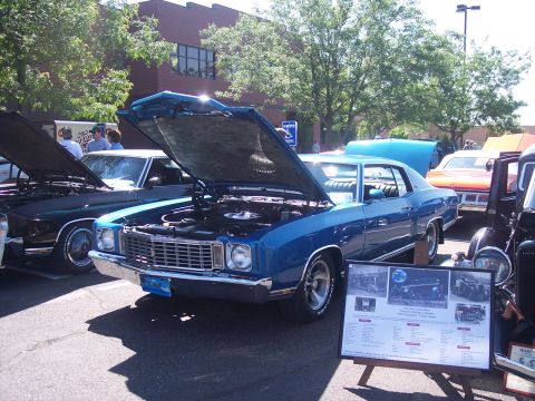 1972 Ford Ranchero - A blue coupe, likely a 1970 Chevrolet Monte Carlo, is displayed with its hood open, alongside other vehicles and an informational board.