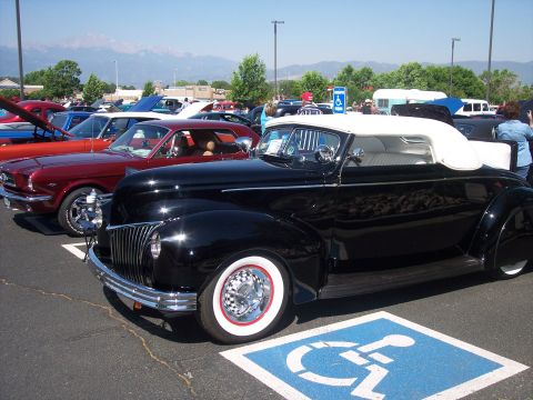 1972 Ford Ranchero - A black convertible from the 1940s is parked in a handicapped spot at an outdoor event.