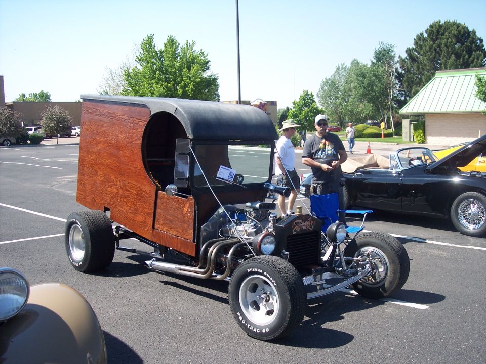 Custom hot rod with wooden box body and exposed engine, parked next to a black convertible
