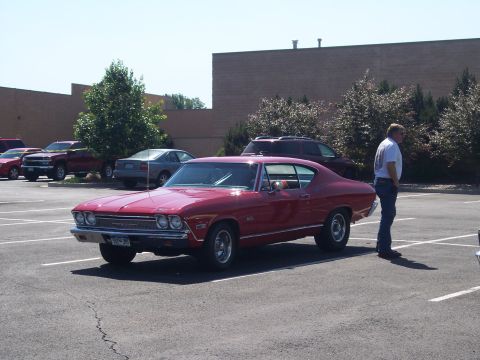 1972 Ford Ranchero - A red 1969 coupe is parked in a lot with a man standing beside it.