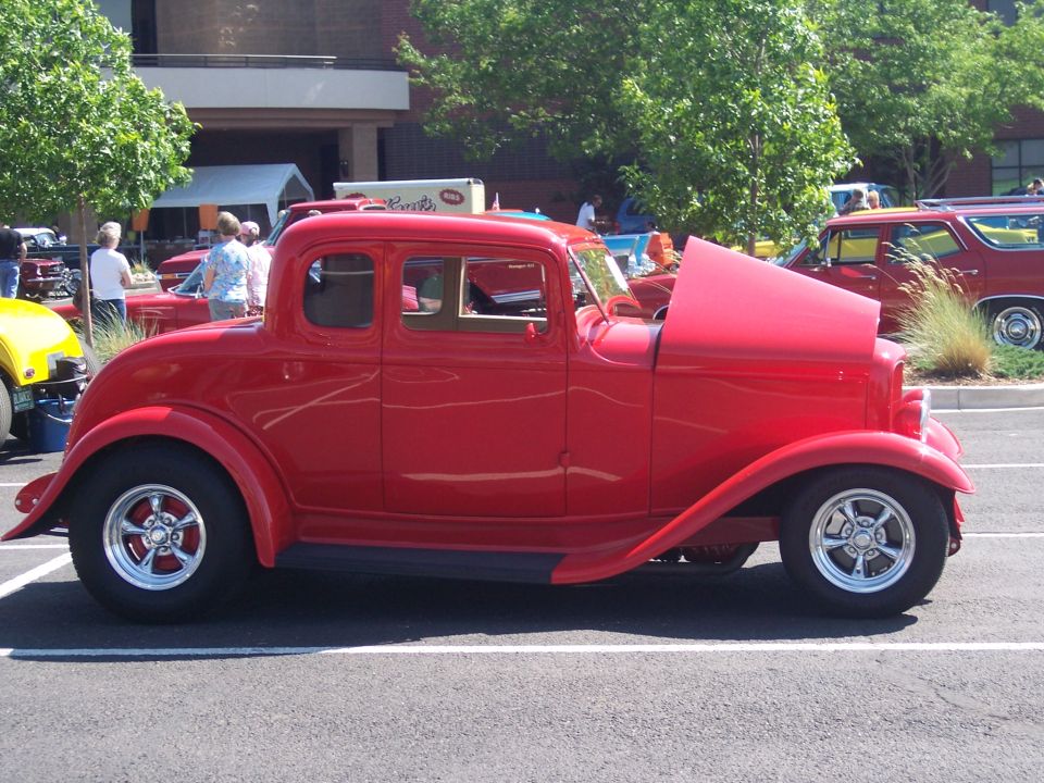 Red 1932 Ford coupe hot rod with hood open, parked next to a red station wagon