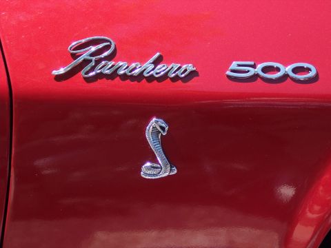 1972 Ford Ranchero - Close-up of chrome "Ranchero 500" script and block badging on a glossy red fender, with a chrome cobra snake emblem mounted below on the bo…