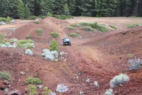 1995 Ford Bronco - A black SUV navigates a , hilly terrain with red dirt and scattered green bushes.