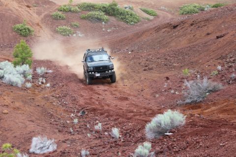 1995 Ford Bronco - SUV navigates a dusty, off-road path through a barren, rocky landscape.